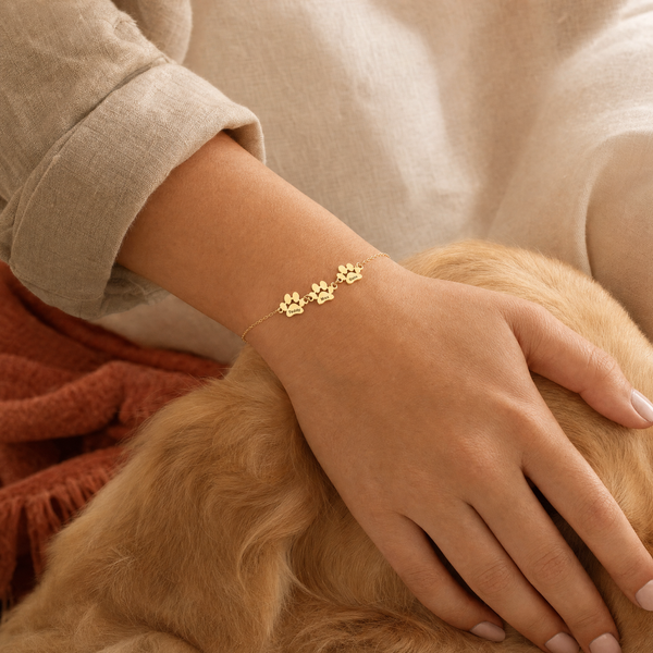 Bracelet Câline en or à 3 pattes gravées Teddy, Max et Oslo, porté au poignet sur un golden retriever